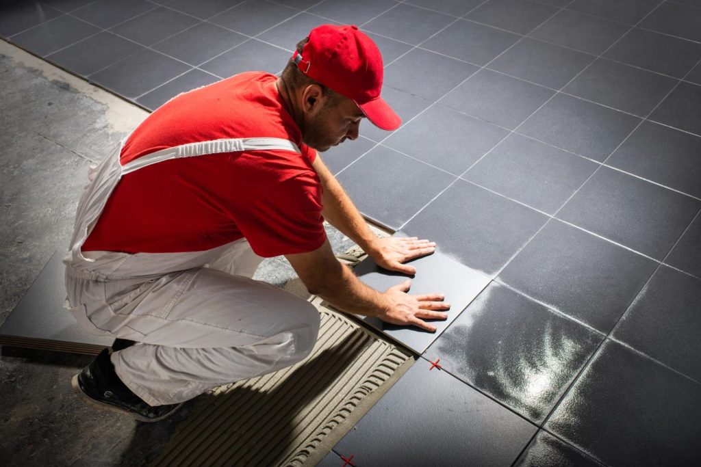A man dressed in red and white is working on laying tiles on a floor, representing flooring services in Columbia, SC.