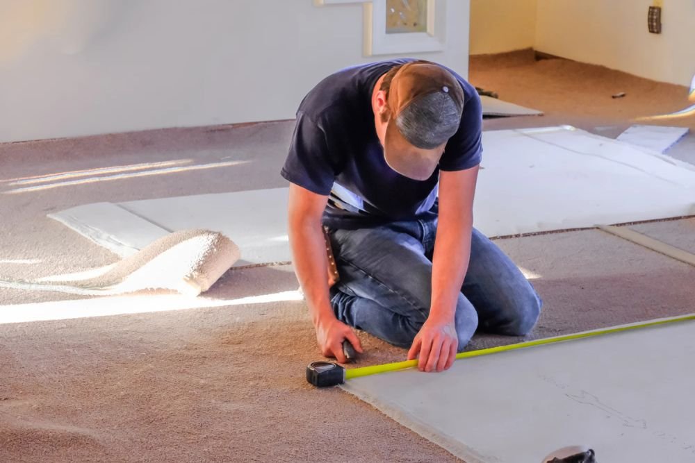 A man working on carpet installation in a room, highlighting carpet tile flooring services in Columbia, SC.