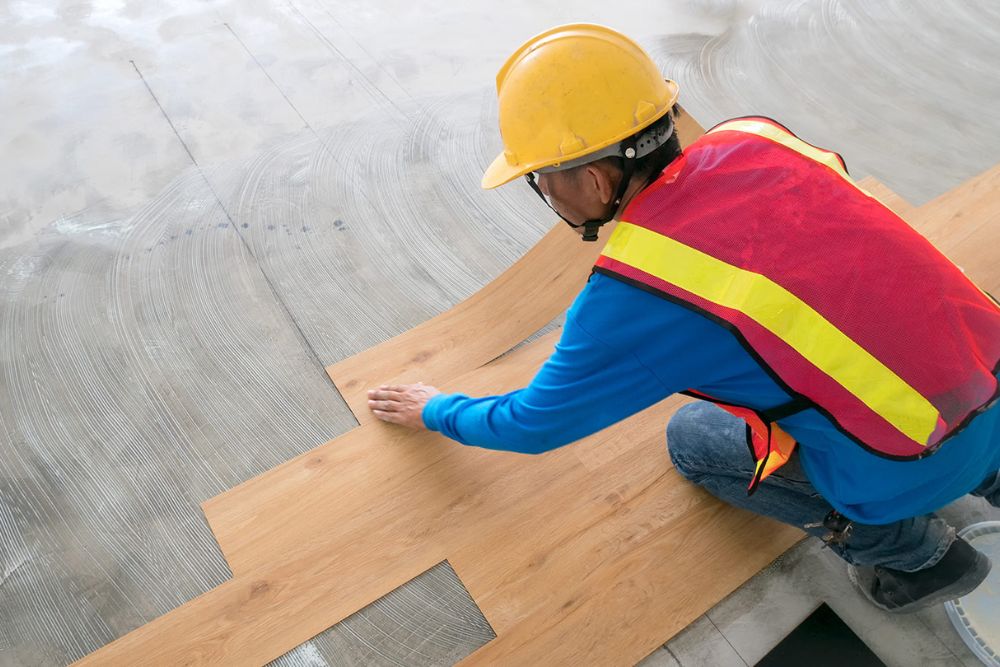 A man in a hard hat and safety vest works on luxury vinyl tile flooring installation in Columbia, SC.