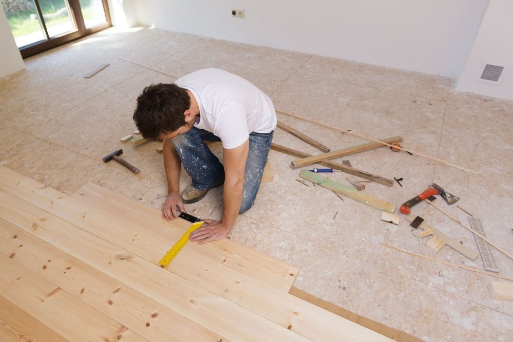 A man works on installing wooden flooring in a room, highlighting hardwood tile flooring services in Columbia, SC.