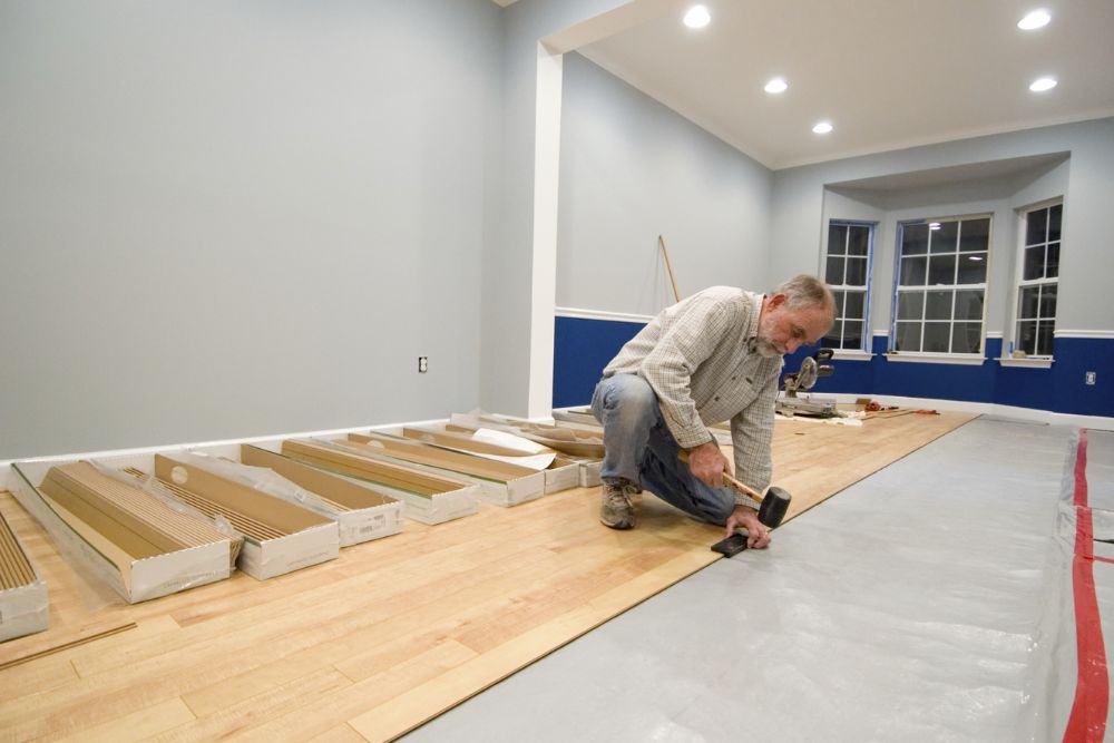 A man works on installing laminate wood flooring in a room, highlighting flooring services in Columbia, SC.