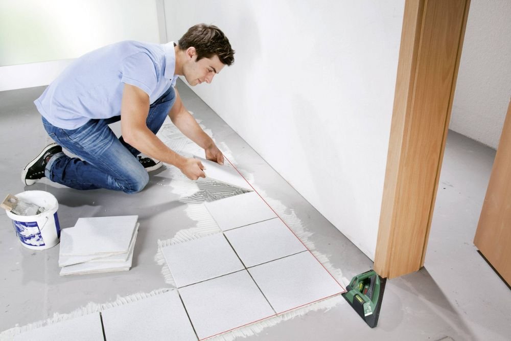 A man applying tiles to the floor, illustrating tile flooring services available in Columbia, SC.