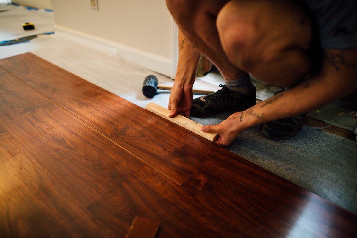 A man carefully installs wooden flooring in a well-lit room, showcasing his craftsmanship and attention to detail.