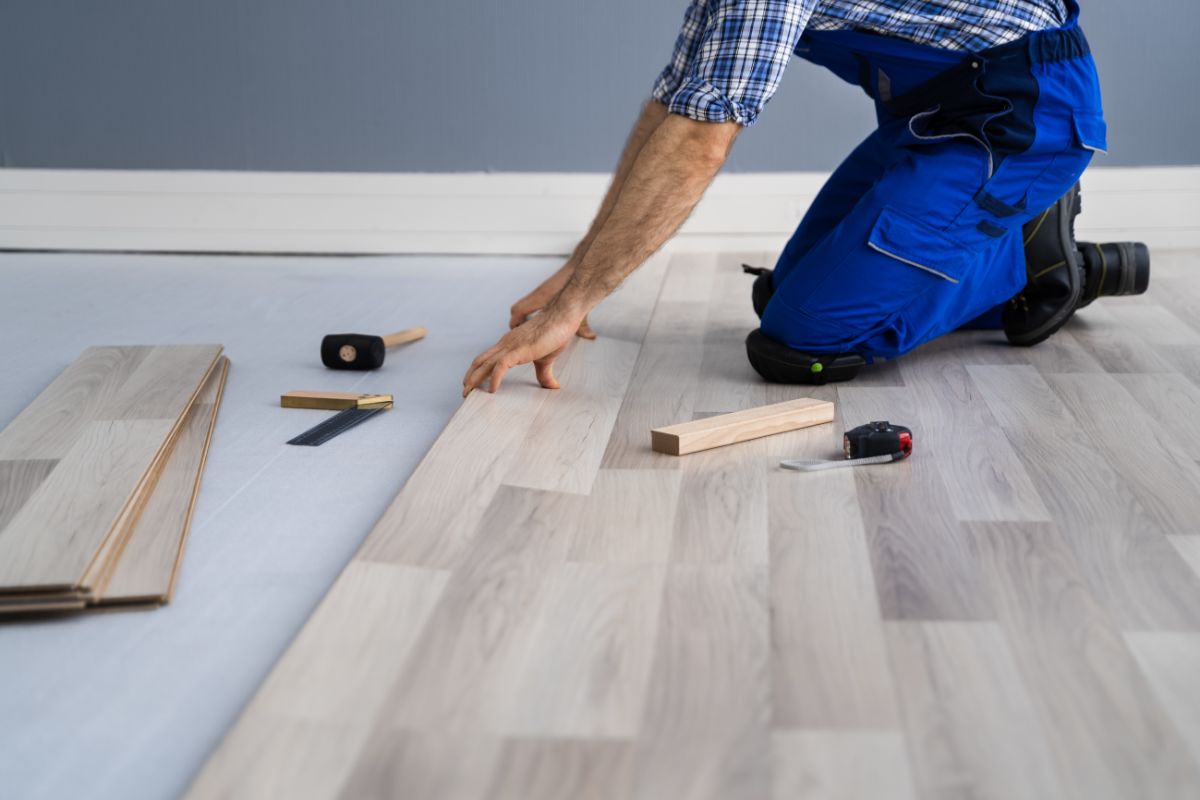 A man is installing wood flooring, carefully laying down each plank in a well-lit room.